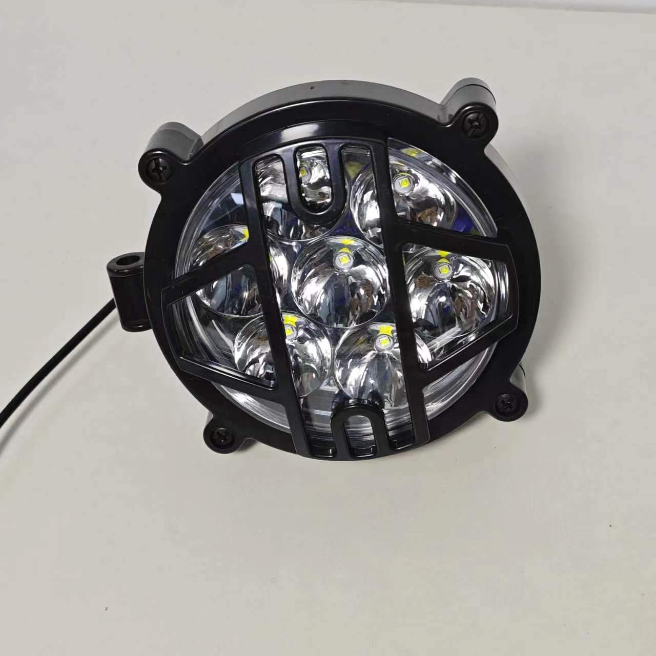 High-intensity LED headlight for electric motorcycles. The headlight is wrapped in a durable black protective grille to ensure safety while enhancing the rugged aesthetic of the vehicle. It features multiple LED bulbs configured in a circular pattern to provide a wide and bright beam, essential for enhanced nighttime visibility and road safety.