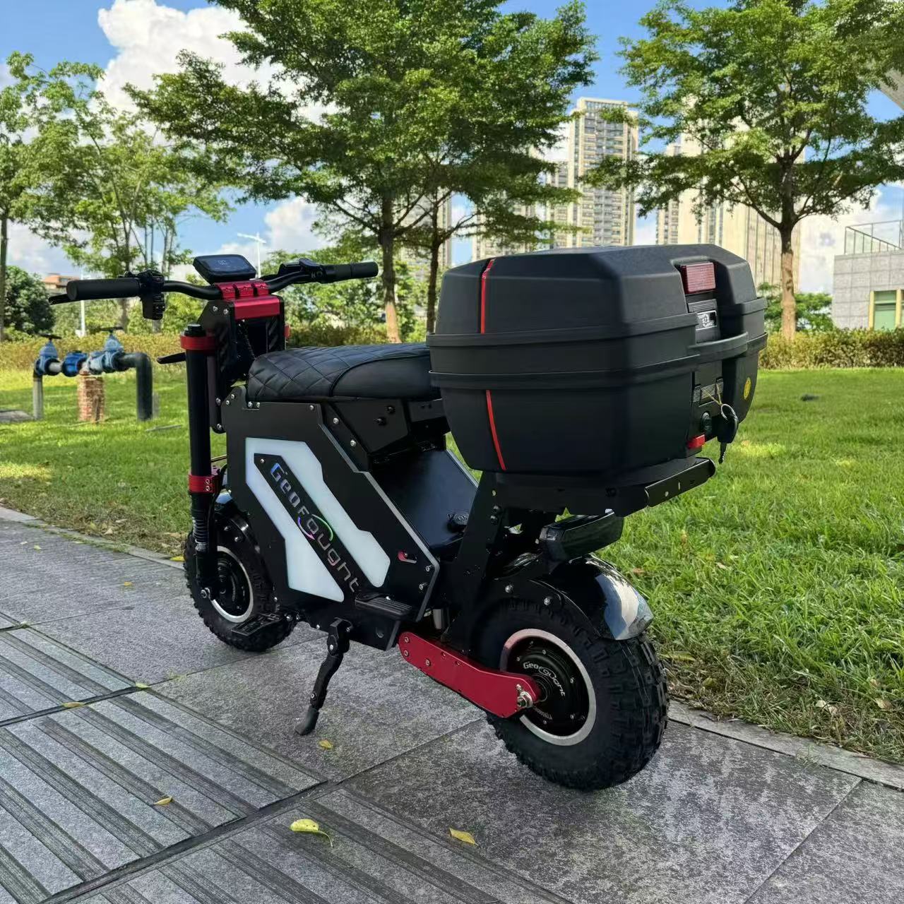 A modified utility electric scooter in black and white with red trim, equipped with off-road tires and a large cargo box. Parked in an urban environment, this scooter is optimized for practicality and comfort on varying terrains.