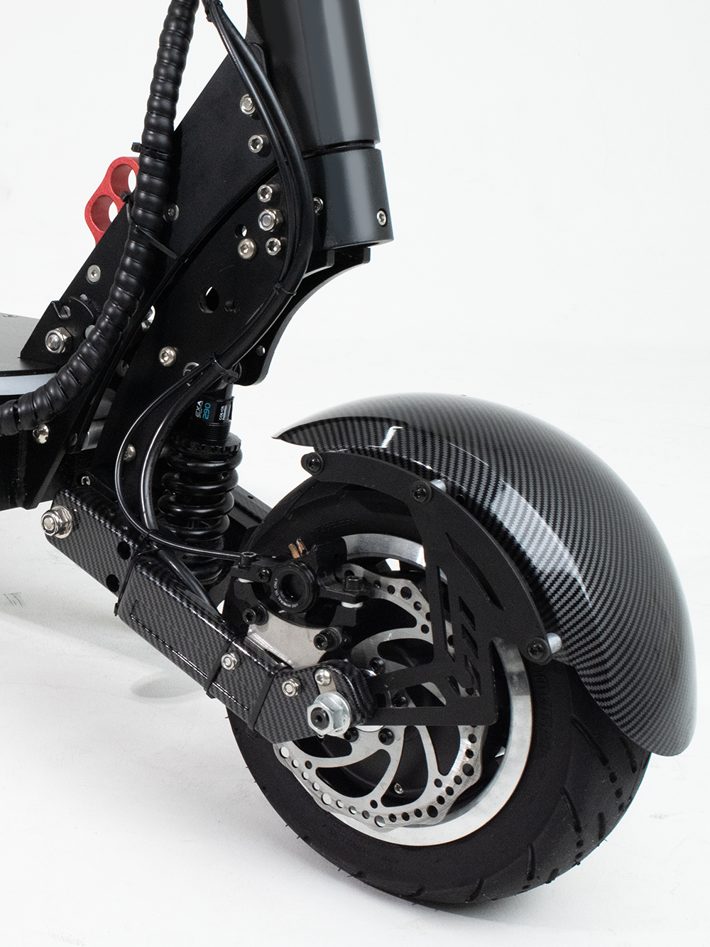 A close-up of the front wheel and suspension system of an electric scooter, featuring a carbon fiber fender, hydraulic shock absorber, and disc brake, engineered for rugged terrain and optimal control.