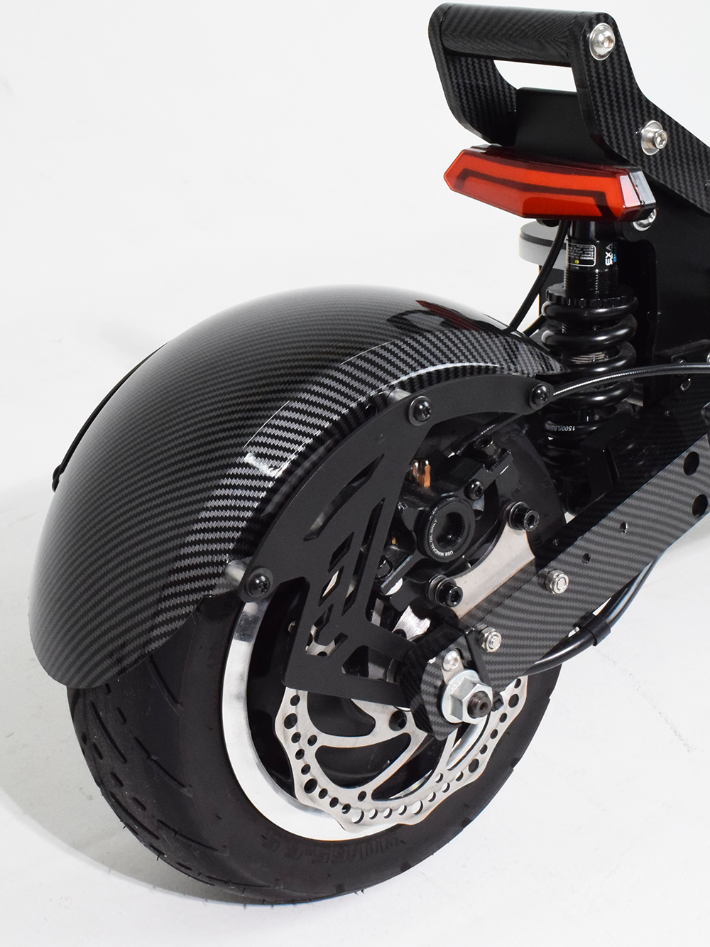  A close-up of the rear wheel and suspension system of an electric scooter, highlighting the carbon fiber fender, disc brake, and shock absorber designed for stability and smooth rides.