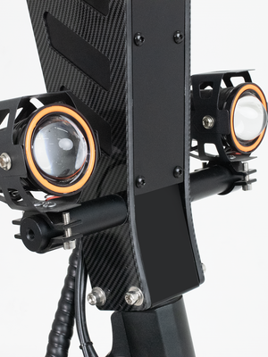 A detailed view of the dual headlights on an electric scooter, mounted on a carbon fiber frame, emphasizing the scooter’s powerful lighting system for enhanced safety and visibility.