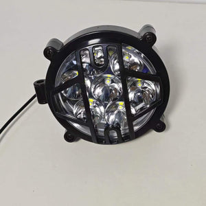 High-intensity LED headlight for electric motorcycles. The headlight is wrapped in a durable black protective grille to ensure safety while enhancing the rugged aesthetic of the vehicle. It features multiple LED bulbs configured in a circular pattern to provide a wide and bright beam, essential for enhanced nighttime visibility and road safety.