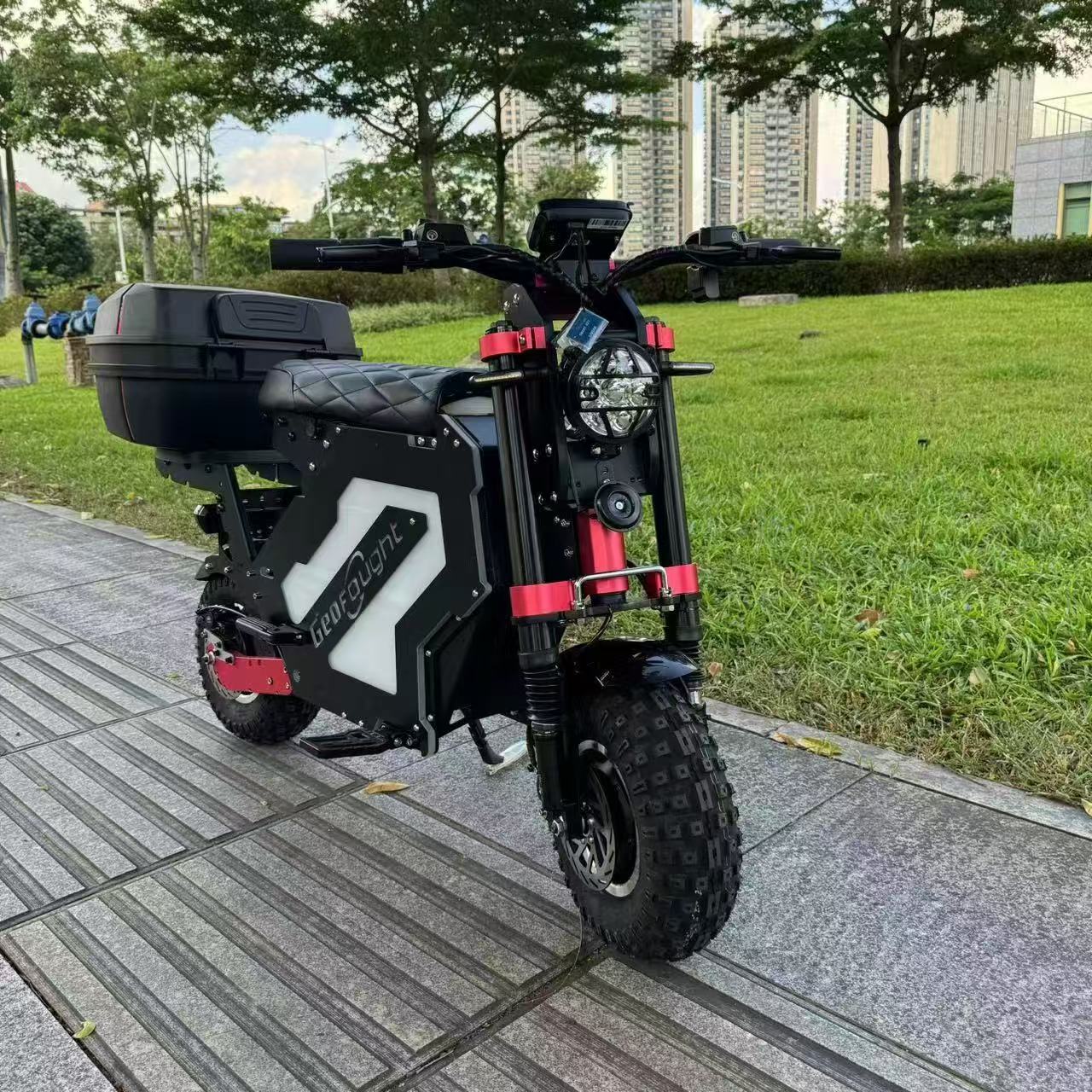 A front view of a mini electric motorcycle designed for off-road use, equipped with a rear trunk, showcased in an urban park setting.