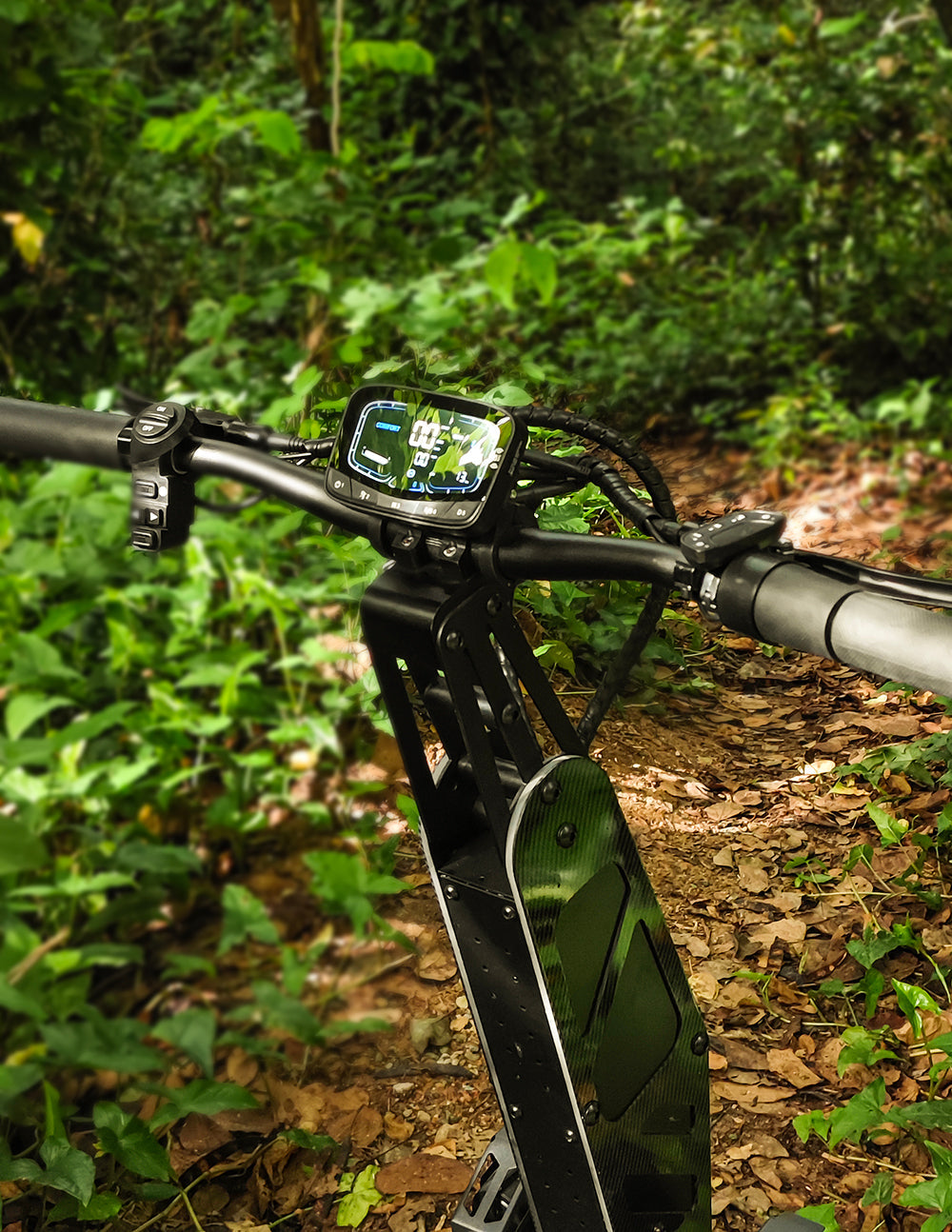 A close-up of the handlebar and digital display of an off-road electric scooter, surrounded by a lush green forest, showing speed and control information.