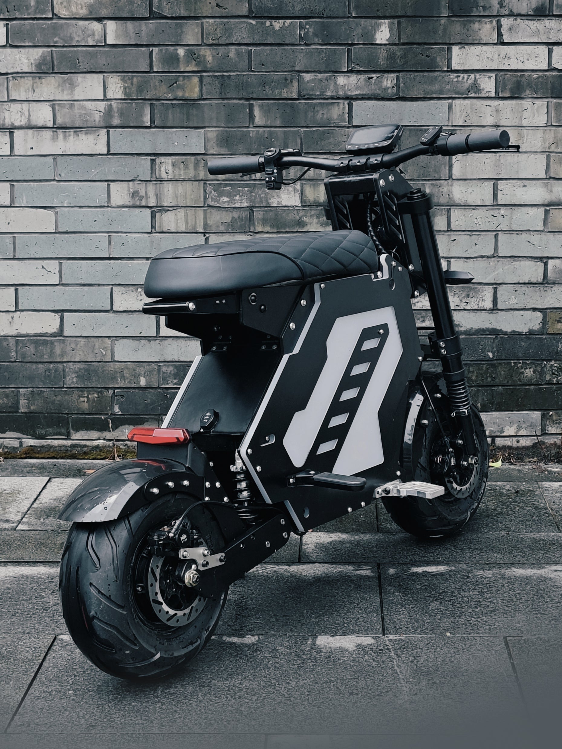 A rear view of an electric motorbike with a compact, futuristic design, parked against a brick wall. The bike features a sturdy build and sleek lines, ideal for urban mobility.