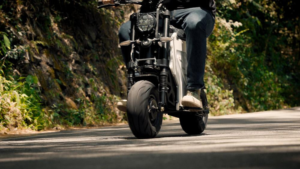 A rider on an electric motorbike cruising on a winding mountain road, emphasizing the vehicle's stability, control, and performance on varied terrains.