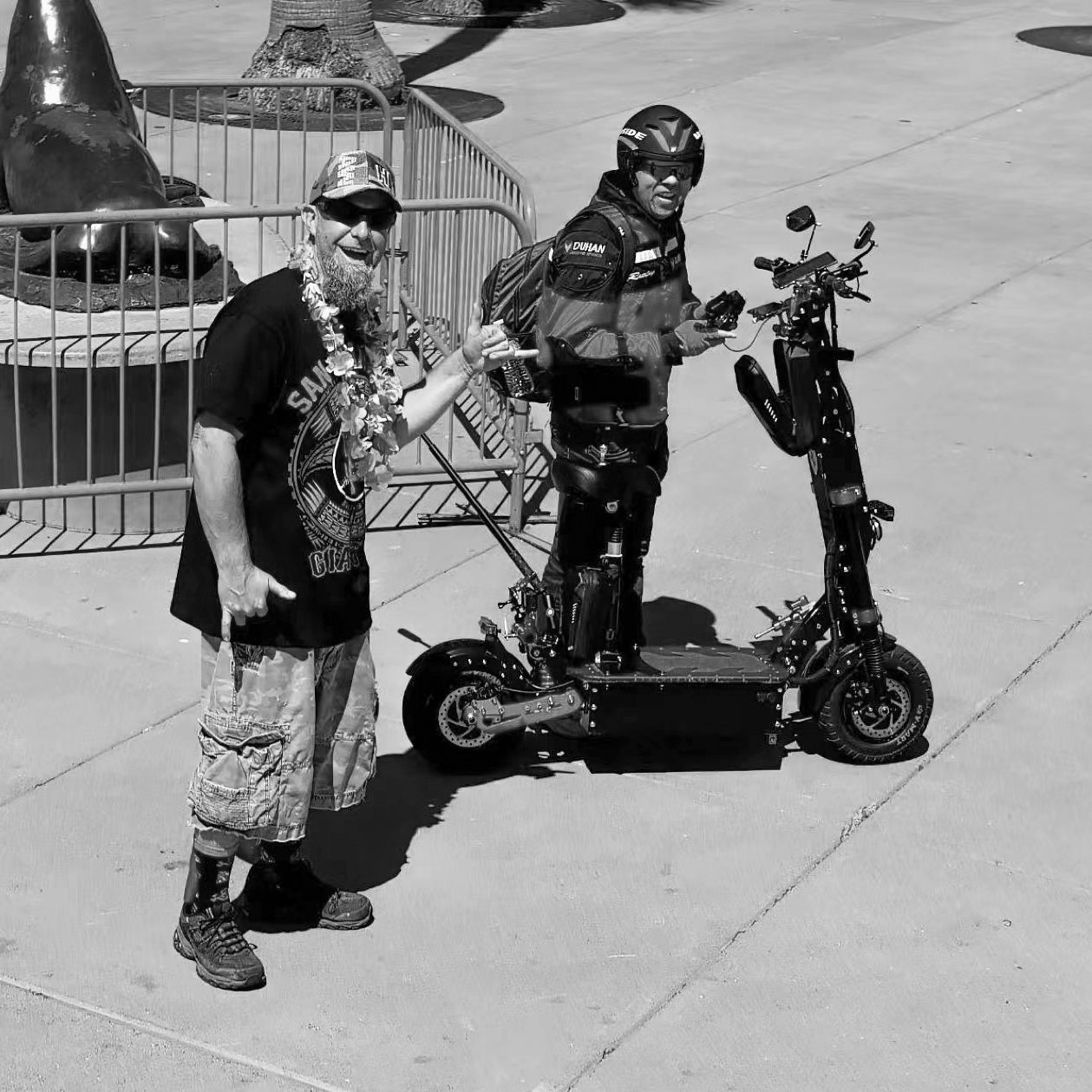 Two men standing with electric scooters in an outdoor plaza. One rider is wearing protective gear, while the other is casually dressed, reflecting the versatility and appeal of electric scooters for different types of riders.